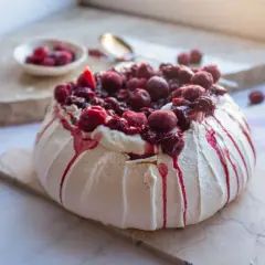 Pyszny tort pavlova z bitą śmietaną i wiśniami, ozdobiony krwistoczerwonym sosem.