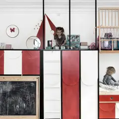 Zwei Kinder teilen sich ein Zimmer mit kreativen Schlafkojen und Spielbereichen. Ein Kind sitzt auf einem Bett, das andere spielt oben.
