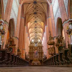 Wnętrze katedry z ceglanymi filarami, bogato zdobionym ołtarzem i rzędami drewnianych ławek. Wspaniały łęg gotyckiej architektury.