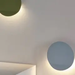Dos lámparas de aluminio circulares, una verde y otra azul, iluminan una pared texturizada.