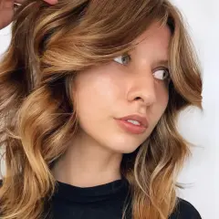 Mujer con cabello castaña iluminada, con ondas suaves y reflejos dorados que resaltan su rostro.