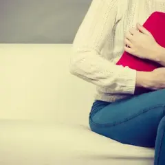Kobieta z termoforem na brzuchu, próbująca złagodzić uczucie pełności w brzuchu.