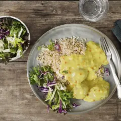 En tallrik med ris, grönsaker och krämiga boller i karry. En skål med sallad står bredvid.
