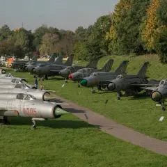 Samoloty wojskowe na trawie w Muzeum Lotnictwa w Krakowie. Widać myśliwce MiG-21 i inne maszyny.