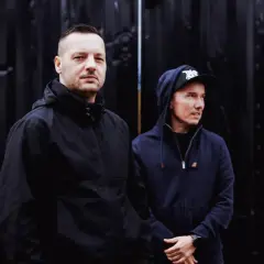 Dwóch członków Paktofoniki, Fokus i Rahim, pozuje na tle czarnej, teksturowanej ściany.