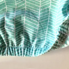 Close-up of a hand demonstrating how to sew in elastic on a teal and white chevron patterned fabric. The elastic creates a gathered, ruffled effect.