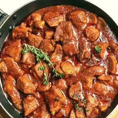 Gicz wołowa duszona w gęstym sosie, ozdobiona gałązkami tymianku, kusi aromatem i apetycznym wyglądem.