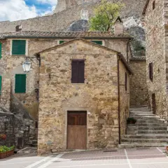 Un vicolo pittoresco a Castel d'Orcia, con case in pietra, persiane verdi e fiori colorati.
