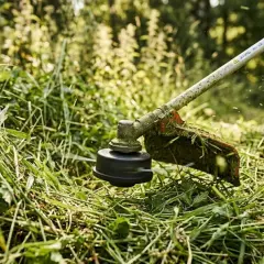 Kosa spalinowa wielofunkcyjna tnie gęstą trawę w słoneczny dzień.