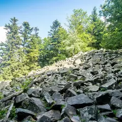 Kamieniste zbocze w Górach Świętokrzyskich, najwyższy szczyt w zasięgu wzroku. Zielone drzewa i błękitne niebo.