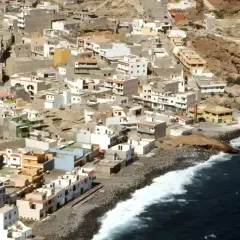 Vista aérea de un pueblo costero en las maretas Tenerife, con casas blancas y de colores apiladas en una ladera rocosa junto al mar azul.
