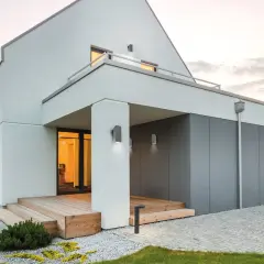 Nowoczesny dom z drewnianym tarasem i podjazdami. Montaż lampy na elewacji podkreśla architekturę.