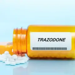 Pomarańczowa buteleczka leku trazodon, z której wysypały się białe tabletki.