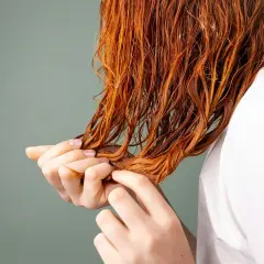 Manos revisando cabello mojado y teñido de naranja, quizás aplicando vinagre para el pelo para brillo y suavidad.