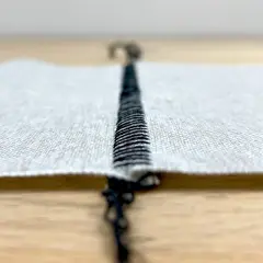 Close-up of a black stitch on white fabric, showing the difference between flatlock and coverstitch techniques.