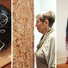 Kula z ciemnej przędzy i wisząca, dwukolorowa tkanina artystyczna. Kobieta ogląda teksturalną instalację.