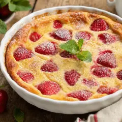Un délicieux clafoutis aux fraises, saupoudré de sucre glace et garni d'une feuille de menthe, prêt à être dégusté.