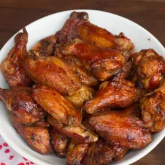 Un bol rempli d'ailes de poulet fumé, nappées d'une sauce brillante et caramélisée, prêtes à être dégustées.