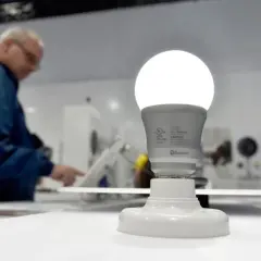 Bombilla fina y brillante en primer plano, con un hombre en segundo plano interactuando con una pantalla.