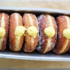 Una fila di bomboloni alla crema, cosparsi di zucchero, pronti per essere gustati.