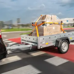 Nowy projekt przyczepki samochodowej UNITRAILER w akcji. Pudełka zabezpieczone pasami na przyczepce ciągniętej przez czarne auto.