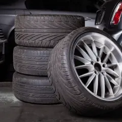 Stos opon gotowych do bieżnikowania, jedna z felgą aluminiową na pierwszym planie.
