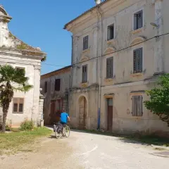 Ciclistas exploran un pueblo antiguo en Croacia, con edificios de piedra y vegetación exuberante.