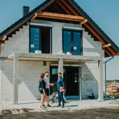 Para młoda wita się z doradcą finansowym przed budowanym domem. Marzenie o własnym gniazdku staje się realne dzięki kredytowi na budowę domu.