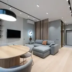 Nowoczesny salon z szarą kanapą i drewnianym stołem. Ściany w odcieniu cool white, jasna podłoga.
