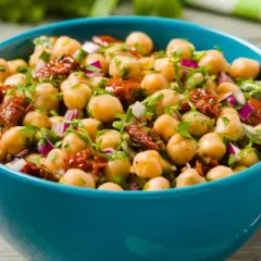 Ensalada de garbanzos fresca y colorida con tomate seco y cebolla morada en un cuenco azul.
