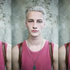 Joven con pelo blanco, viste camiseta rosa y un collar con un amuleto.