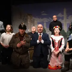 Aktorzy na scenie, w strojach z epoki, tworzą teatr ciut frapujący. W tle malowana miejska panorama.