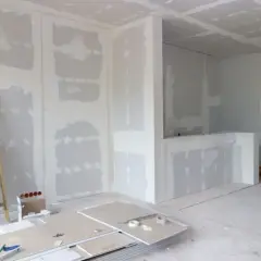 Interni in fase di finitura, con pareti in cartongesso pronte per essere stuccate. Una scala appoggiata al muro, pannelli e attrezzi a terra suggeriscono come fare un muro.