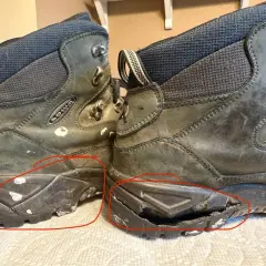 Two worn hiking boots with cracked and damaged soles, highlighted by red circles.