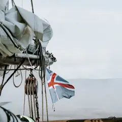 Szot grota powiewa na wietrze, ukazując maszty i liny statku żaglowego na tle mglistych gór.