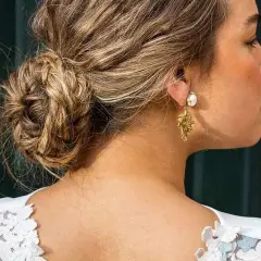 Elegante recogido pelo rizado boda invitada, con un moño trenzado y pendientes dorados.