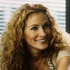 Julia Roberts z burzą blond loków, uśmiechnięta, jakby opowiadała historię z filmów na faktach.