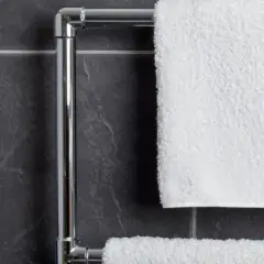 En handdukstork i krom hänger på en mörk kaklad vägg. En vit, fluffig handduk är upphängd.