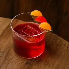 Elegancki Negroni Sbagliato z kostką lodu i ozdobą z pomarańczy i czerwonych owoców na drewnianym blacie.