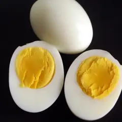 Un œuf entier et deux moitiés d'œufs durs sur fond noir, montrant le jaune bien cuit. Parfait pour une salade ou un en-cas.
