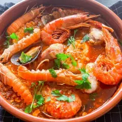 Deliciosa zarzuela de pescado con gambas, mejillones y cigalas en una cazuela de barro, decorada con perejil fresco.
