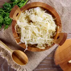 Holzschale mit Sauerkraut, daneben ein Holzlöffel und Petersilie. Sauerkraut gesund und lecker!