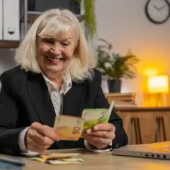 Uśmiechnięta starsza pani liczy pieniądze, zastanawiając się, ile wynosi opiekuńcze na starszą osobę.