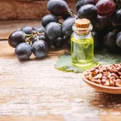 Racimos de uvas oscuras junto a una botella de aceite y una cuchara con semillas, mostrando el origen del extracto de semilla de uva.