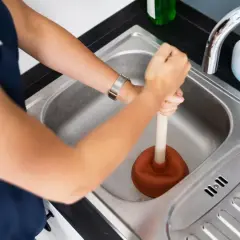 Une personne utilise une ventouse pour déboucher la canalisation d'eau chaude de l'évier.