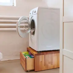 Waschmaschinen Podest selber bauen: Eine weiße Waschmaschine steht auf einem Holzpodest mit Schublade, darin Waschmittel.