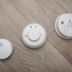 Trois détecteurs de fumée blancs sur un parquet. L'obligation d'installer un détecteur de fumée en entreprise est une mesure de sécurité essentielle.