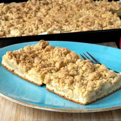 Zwei Stücke saftiger Apfelkuchen mit Streuseln auf einem blauen Teller, daneben ein ganzer Apfel. Perfekt für ein Apfelkuchen Rezept.