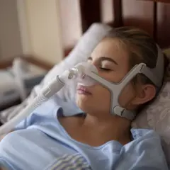 Kobieta śpi z maską CPAP, która pomaga na bezdech senny. Urządzenie zapewnia spokojny oddech przez całą noc.