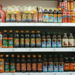 Rayons de supermarché remplis de bouteilles de thé glacé, de jus et de boissons. On y trouve des marques comme Lipton, Nestea et C2. Certaines bouteilles contiennent du bicarbonate dans l'eau pour une touche pétillante.